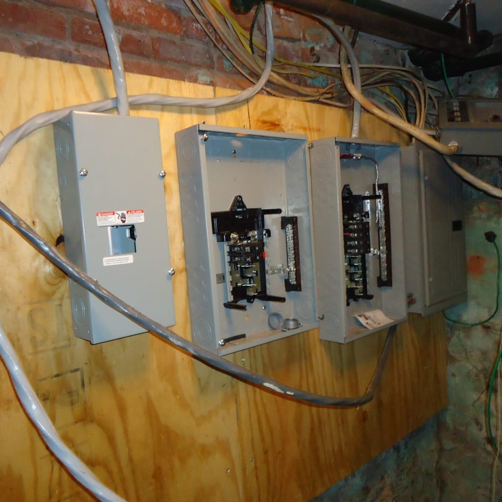 Open breaker panels mounted on plywood in an older brick basement