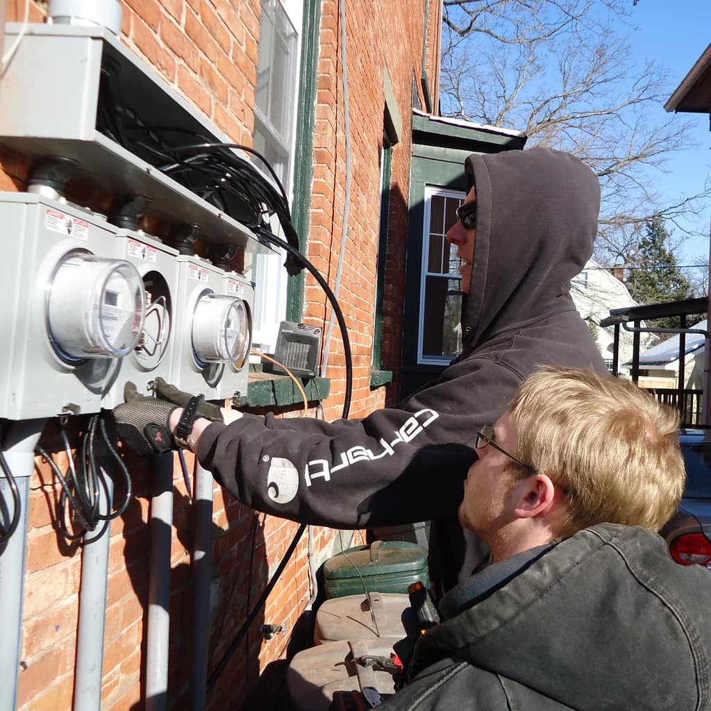 Electricians fitting meter panels on the outside wall of a brick house